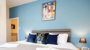 Ein Hotelzimmer mit Bett, Kopfteil, einem Bild an der Wand und einer Tür zu einem anderen Raum.