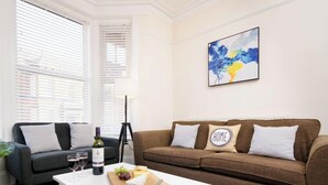 Ein Wohnzimmer mit einer dunkelgrauen Couch, einer braunen Couch und einem weißen Couchtisch mit einer Weinflasche, Gläsern und Käse.