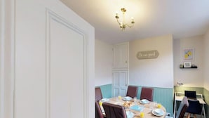 Un coin repas avec une table dressée pour quatre personnes, un lustre et une pancarte sur laquelle on peut lire : « Soyez nos invités ».