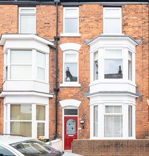 A two-story brick house with bay windows, a red door, and a white car parked in front. - Scarborough Stays Trafalgar Lodge (North Yorkshire)