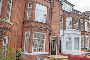 A red brick building with a bay window, a door labeled '127', and a round wooden table outside.