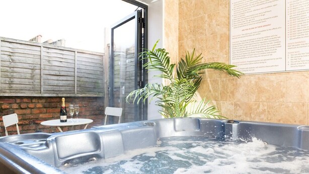 Un bain à remous avec une table et des chaises à l’extérieur, une plante en pot et un menu affiché au mur.