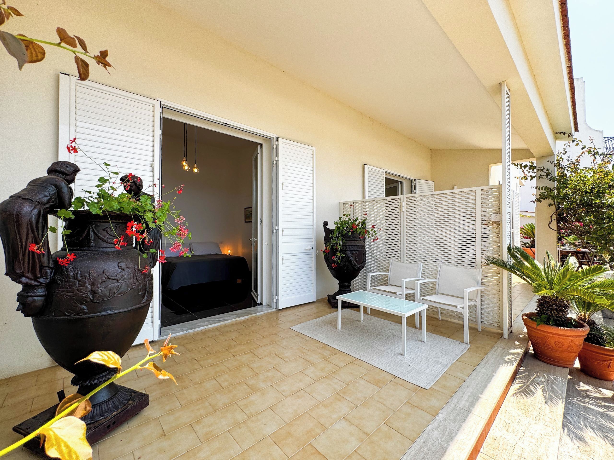 Ein Balkon mit Sitzgelegenheit, einem großen Dekokübel und einer Schiebetür zu einem Zimmer.