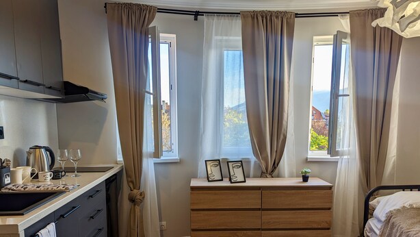 A modern bedroom with a wooden dresser, a bed, and a view of the outdoors through a window. - Lily's Studio 4 by Bulgarentals - Central Sofia (Sofia)
