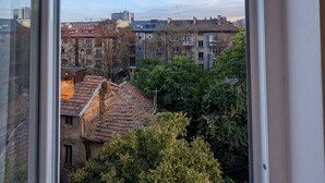 A view from a window overlooking a cityscape with buildings and trees. - Lily's Studio 4 by Bulgarentals - Central Sofia (Sofia)