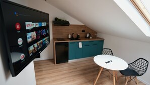 A modern kitchen with teal cabinets, a black dishwasher, and a white dining table with black chairs.