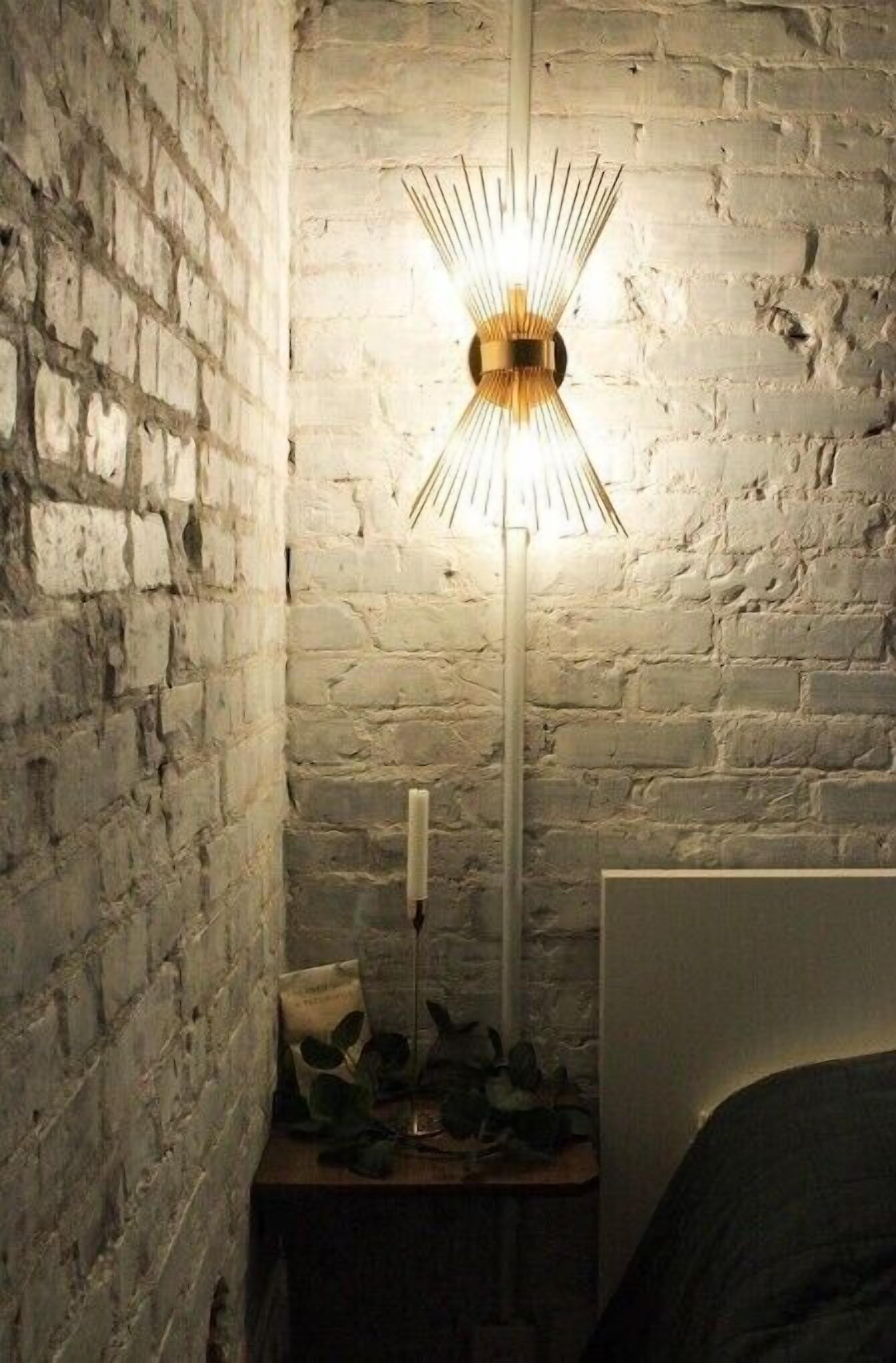 Una habitación con pared de ladrillo, una lámpara de pie moderna, una mesita de noche con una vela y una cama.