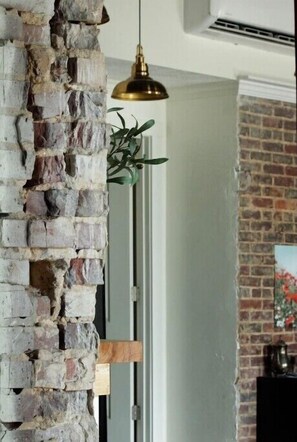A brick wall with a hanging pendant light, a door, and a brick fireplace with a painting. - La Banque Stylish and comfy stay
 (Finger)