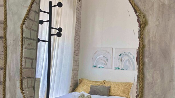 A bedroom with a bed, a mirror, and a window with curtains.