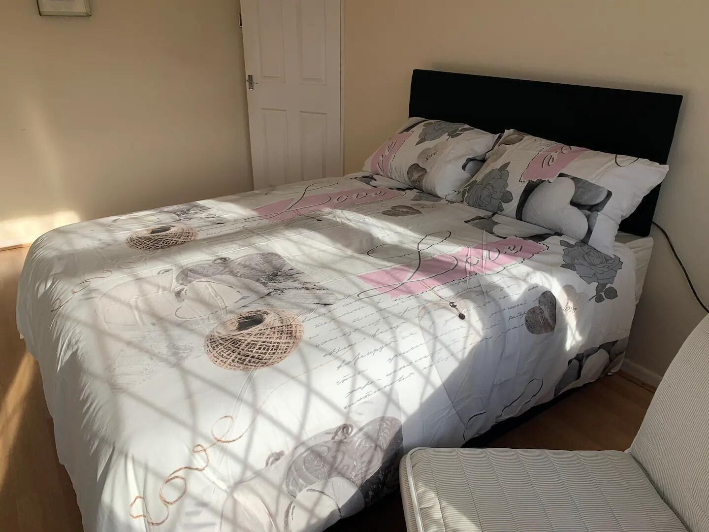 Un lit bien fait, recouvert d’une couvre-lit aux motifs floraux et géométriques, avec une tête de lit noire et une table de chevet sur laquelle se trouve une lampe.