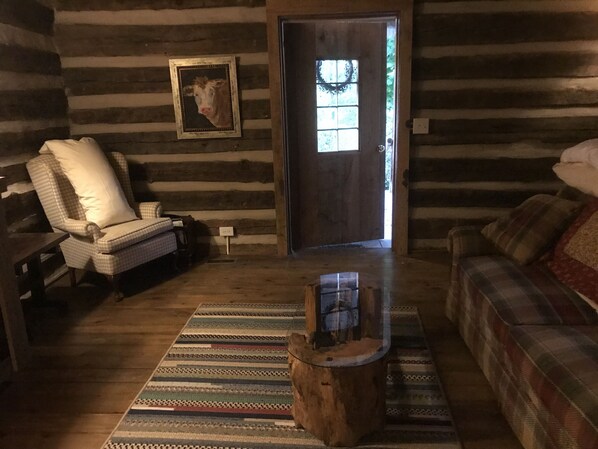 Interior de una cabaña de troncos con un sillón a cuadros, un sofá escocés, una mesa de centro de madera y un cuadro en la pared.