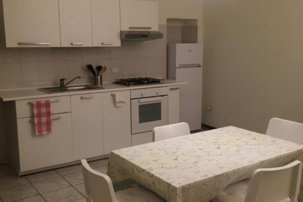 A compact kitchen with white cabinets, a gas stove, a microwave, and a refrigerator. There is a dining table with four chairs.