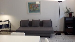 Een woonkamer met een grijze bank, een witte tafel en een vloerlamp.
