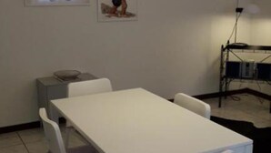 Een kamer met een witte tafel, twee stoelen, een klein kastje en een poster aan de muur.