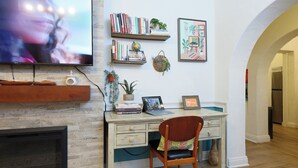 Ein Homeoffice mit Kamin, einem Schreibtisch mit Laptop, Bücherregalen und einem an der Wand befestigten Fernseher.
