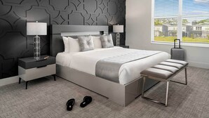 A modern bedroom with a large bed, two bedside tables with lamps, a bench, and a suitcase.