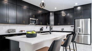 A modern kitchen with dark cabinets, stainless steel appliances, a white island, and bar stools. - The Magical | Unbelievable wizard theme BR & more magical RMs, near Harry P Land (Orlando)