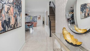 A spacious hallway with a staircase, modern art on the walls, and a dining area in the background. - The Mystical | Ocean-lover's home w PVT pool, submarine theme BR, near waterpark (Orlando)