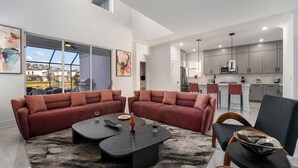 A modern living room with a sectional sofa, a coffee table, and a view of the kitchen. - The Mystical | Ocean-lover's home w PVT pool, submarine theme BR, near waterpark (Orlando)