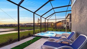 Un espace piscine doté de chaises longues et d’un jacuzzi, le tout entouré d’une structure en verre offrant une vue sur un quartier résidentiel.