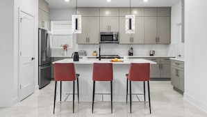 A modern kitchen with a central island, stainless steel appliances, and red bar stools.