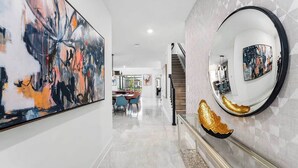 A modern hallway with a marble floor, a staircase, and a dining area in the background.