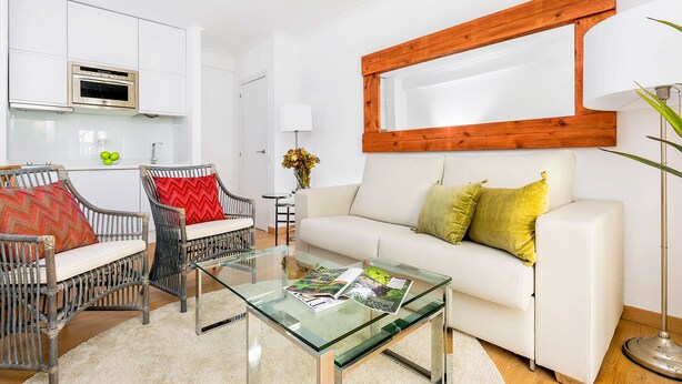 A modern living room with a glass coffee table, wicker chairs, a white sofa, and a wooden-framed mirror. - Genteel Home Placentines (Seville)