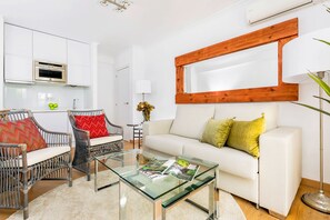 Un salón moderno con una mesa de centro de vidrio, sillas de mimbre, un sofá blanco y un espejo con marco de madera.