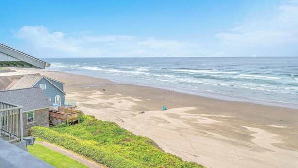 A beach view with a house and a wooden deck. - Oceanfront Condo Amazing Views, Charming Nautical Theme, Covered Deck (Newport)