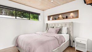 Een slaapkamer met een groot bed, een nachtkastje, een raam en een plank met decoratieve objecten.
