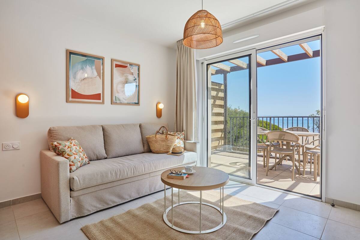 A modern living room with a sofa, a round table, and a balcony with outdoor furniture.