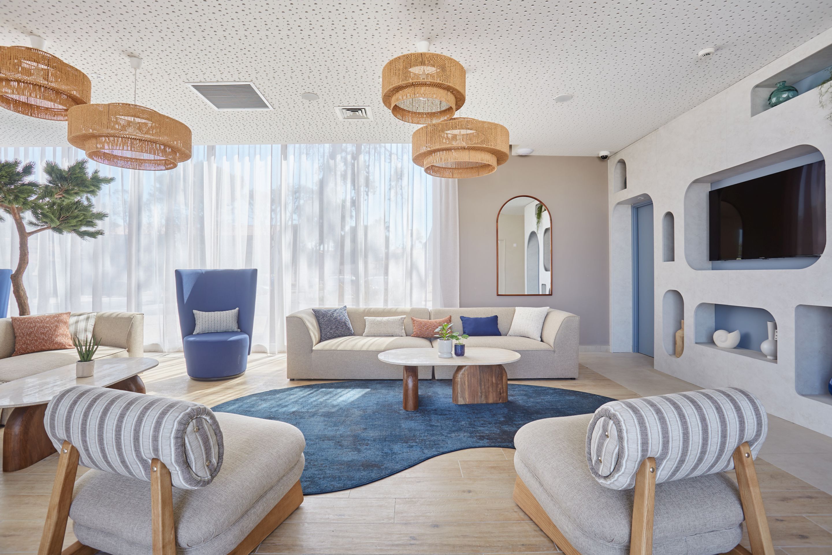 A modern living room with a sofa, armchairs, a coffee table, and a large window with sheer curtains.