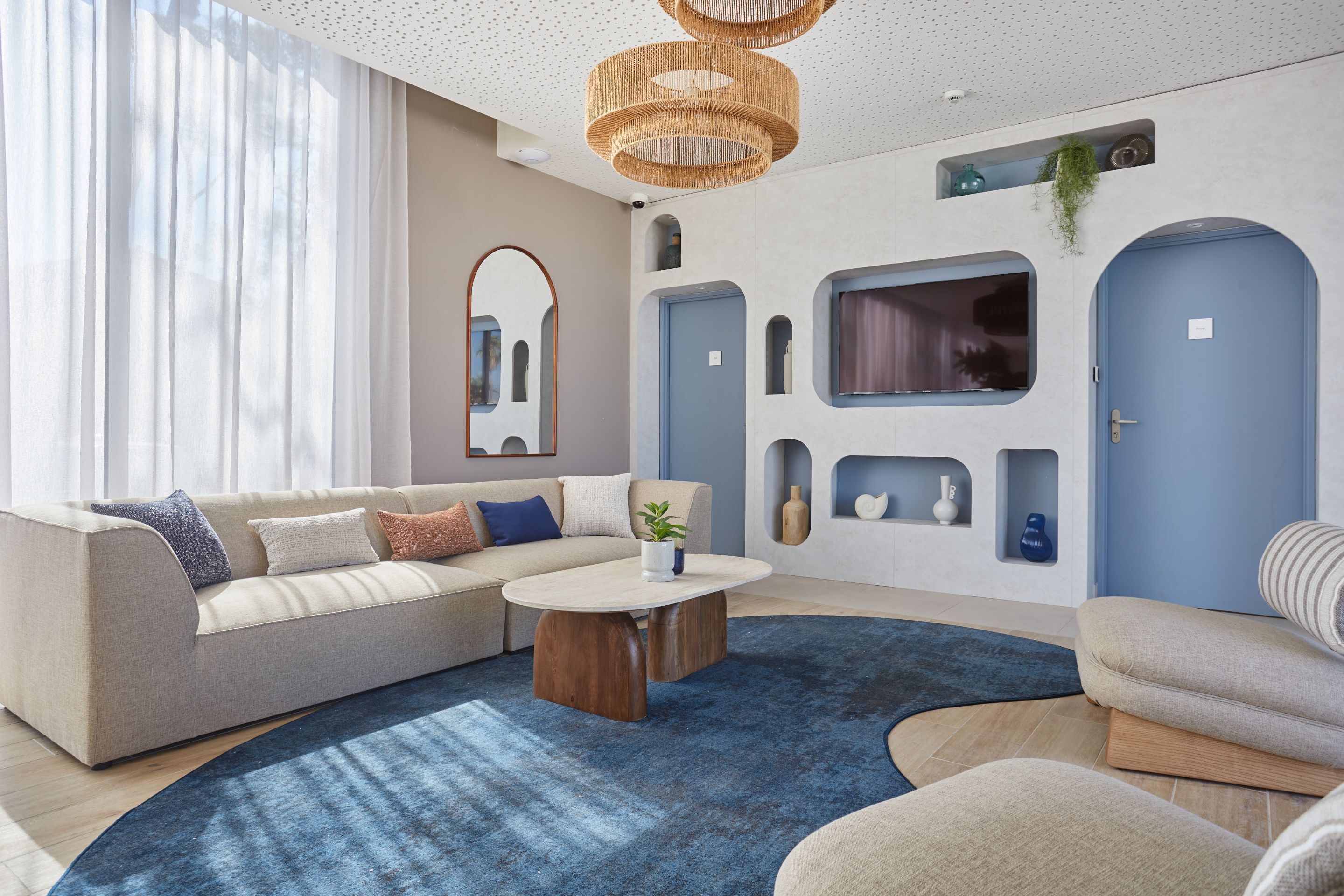 Een moderne woonkamer met een bank, salontafel en een blauw vloerkleed. Er zijn twee deuren en een spiegel aan de muur.
