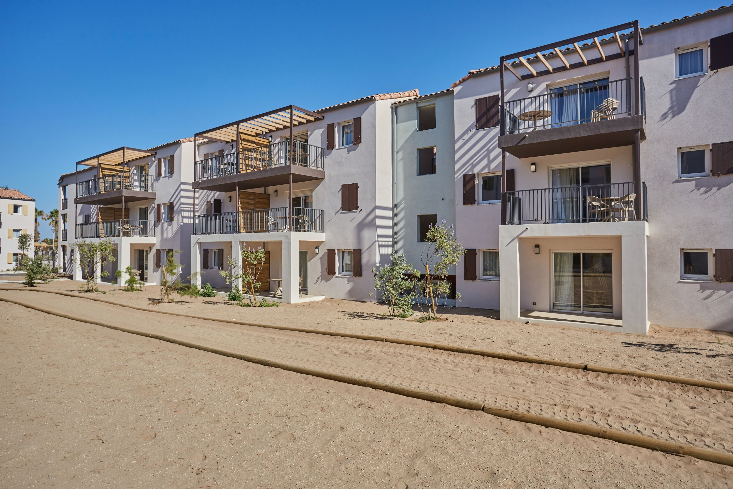 A row of modern apartment buildings with balconies, some with wooden pergolas.
