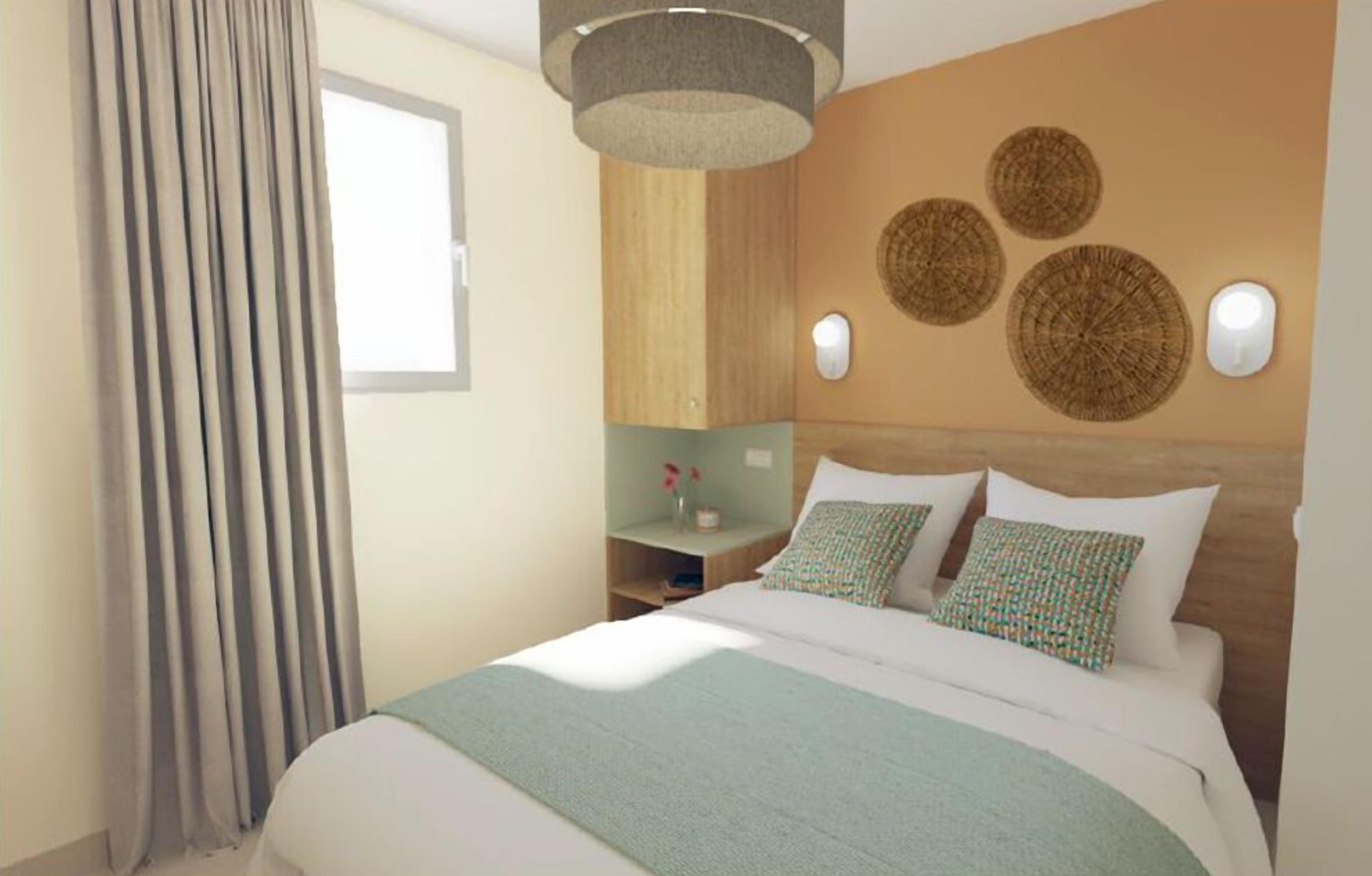 Een hotelkamer met een bed, nachtkastje, een wandlamp en een raam met gordijnen.