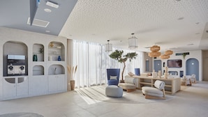 A modern living room with a kitchen area, featuring built-in cabinets, a dining table, and a large window with sheer curtains. - Résidence Odalys Riviera la Presqu'Ile (Hyères)