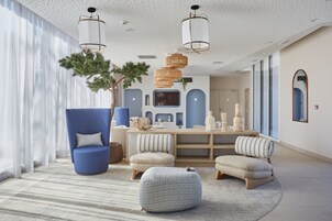 Una sala moderna con un sillón azul, un reposapiés redondo y una mesa de centro de madera.
