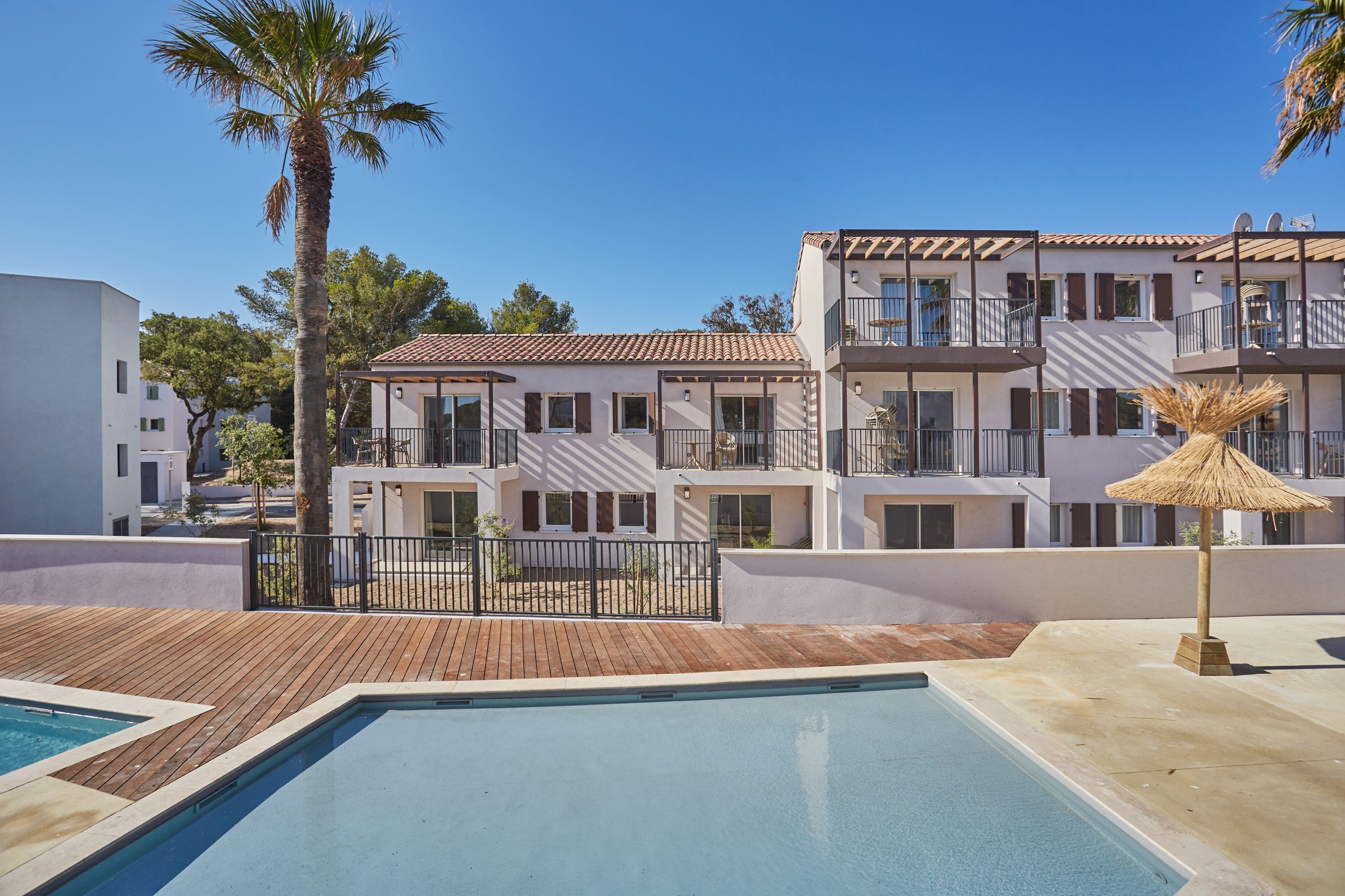 A pool area with a wooden deck, a palm tree, and a building with balconies.