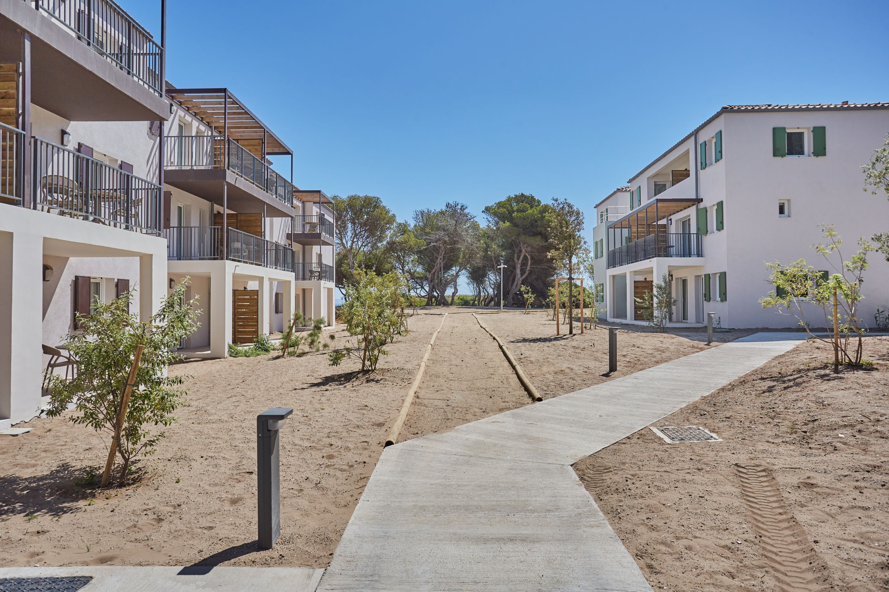 A residential building with multiple balconies, a sandy ground, and a clear sky.