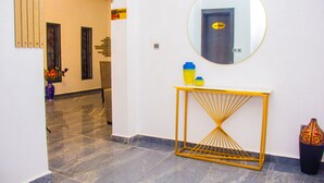 Un couloir doté d’un sol en marbre, d’un grand miroir rond accroché au mur, et d’une console jaune sur laquelle sont posés un vase et une bouteille.