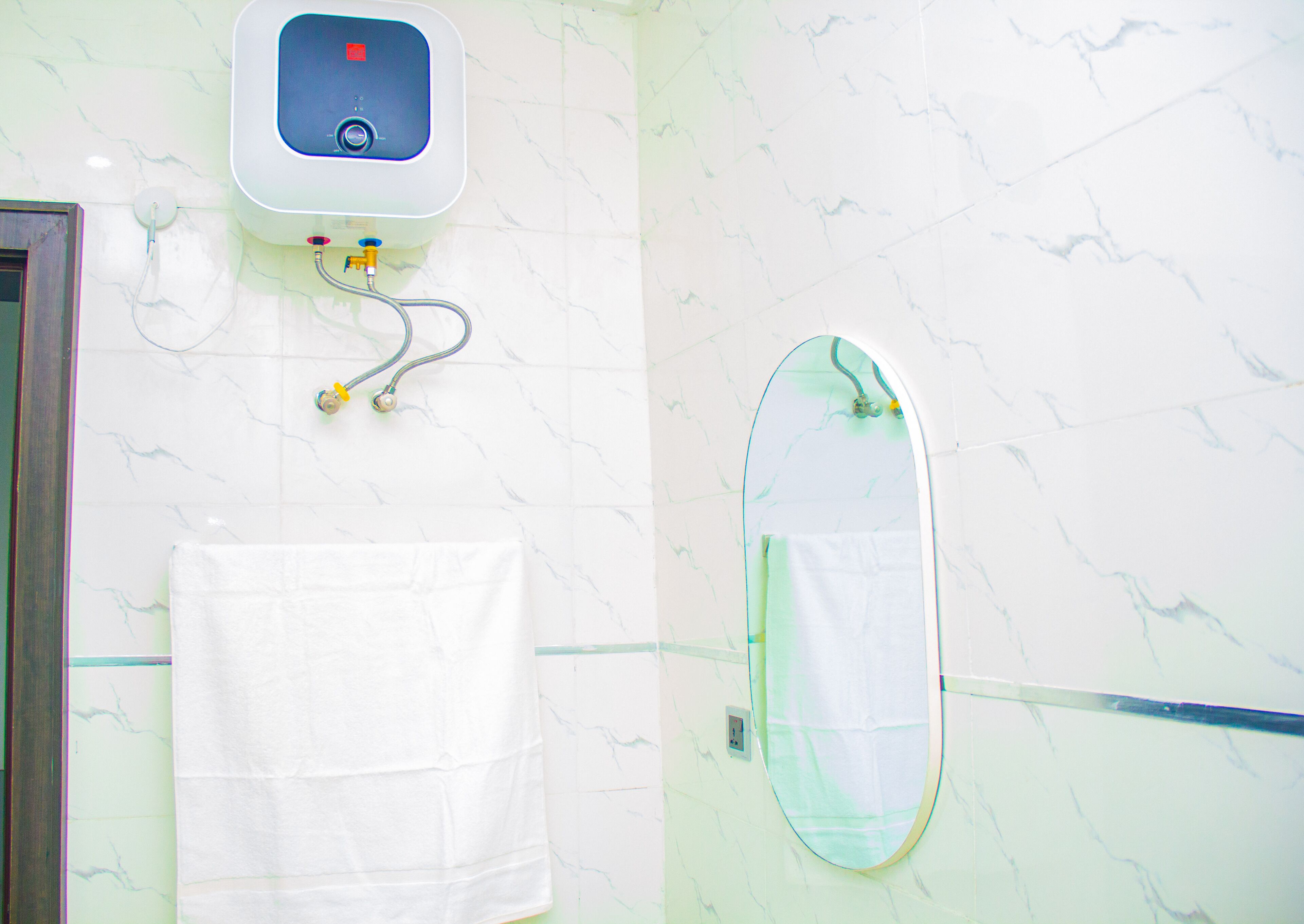 A bathroom with a white marble wall, a towel rack with a white towel, a handheld showerhead, and a wall-mounted soap dispenser.