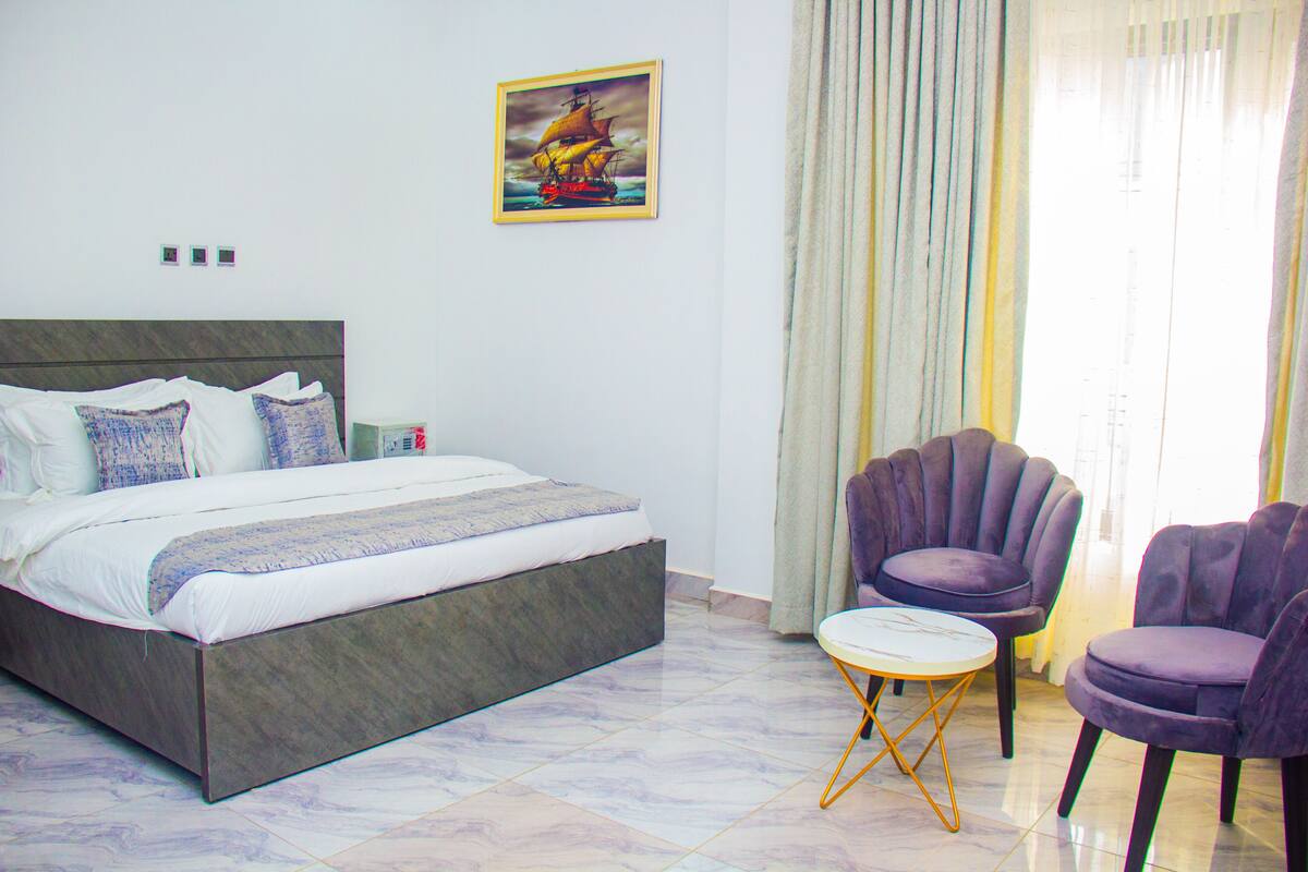 Une chambre à coucher avec un lit, une petite table, deux chaises et un tableau accroché au mur.