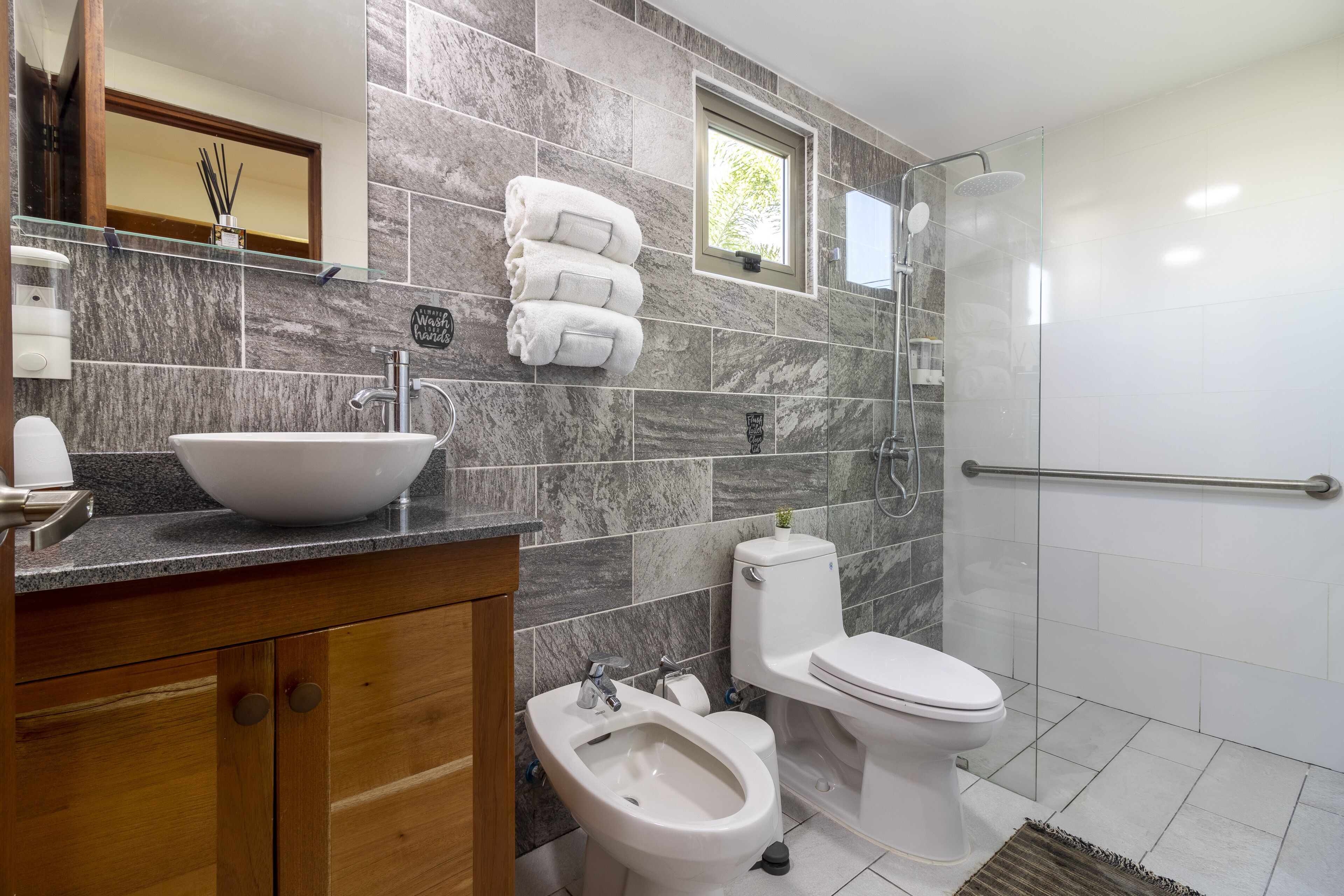 Un baño moderno con salpicadero de mármol, cabina de ducha con mampara de vidrio, un bidé, un inodoro y un lavabo con lavamanos integrado.