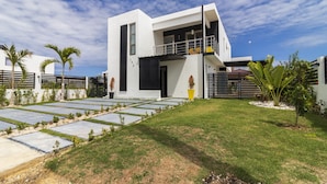 A modern two-story house with a flat roof, a balcony, and a well-maintained lawn. - Modern 4-BR Villa in Gated Community (Punta Cana)