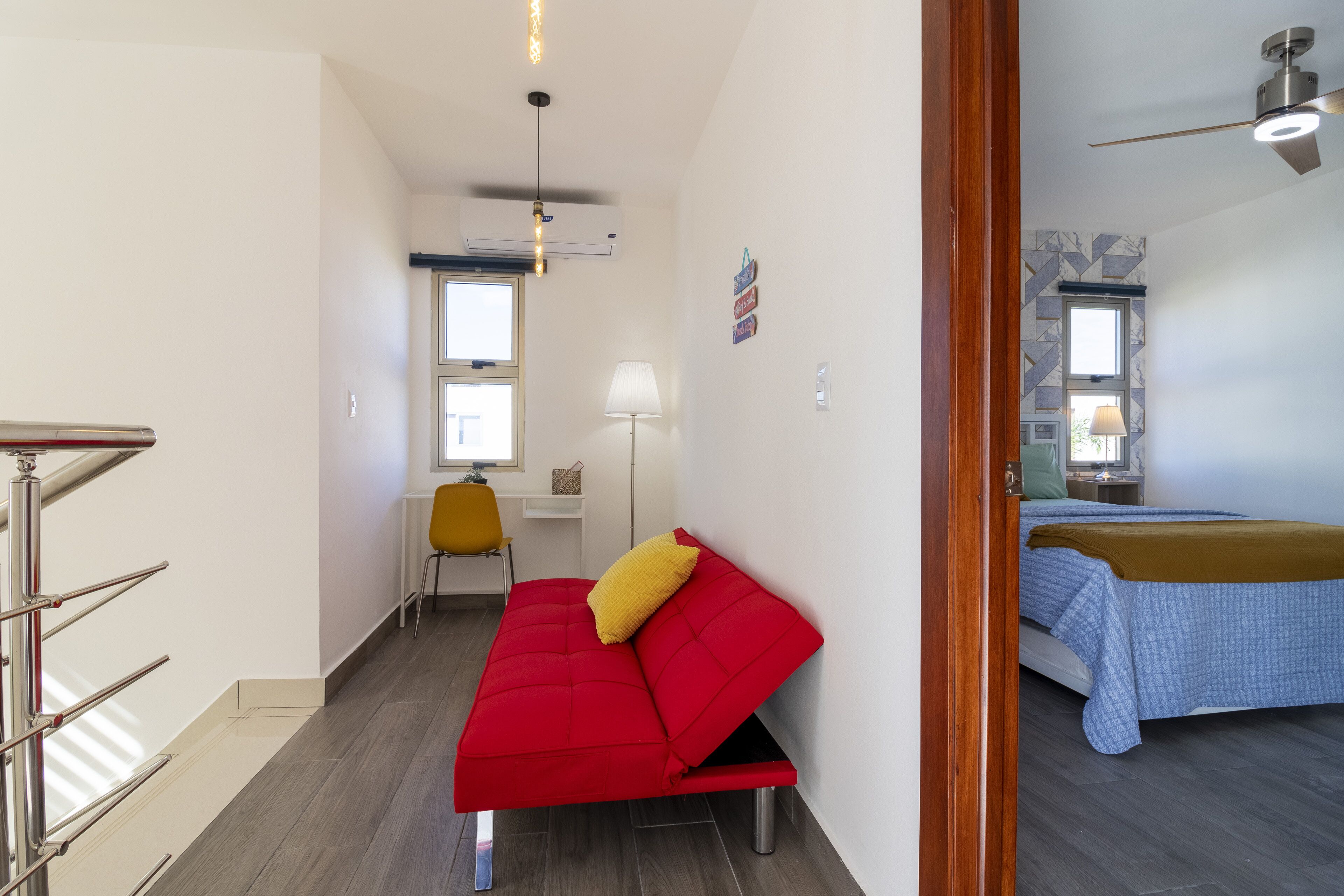 Ein kleiner Wohnraum mit einem roten Sofa, einem kleinen Tisch, einer Lampe und einem Bett mit blauer Bettdecke.