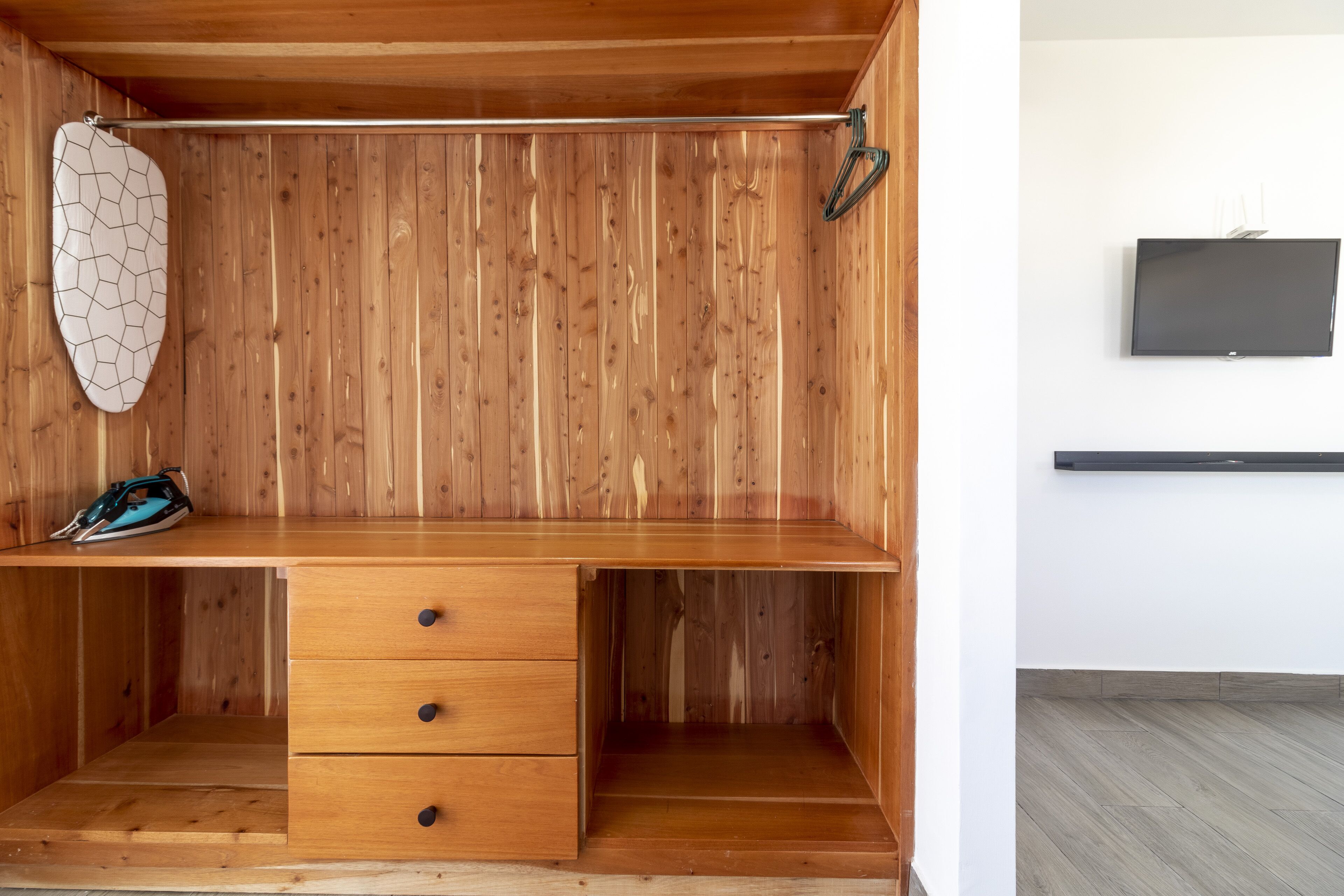 A wooden desk with drawers, a hanging coat rack, and a pair of shoes.
