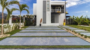 A modern two-story house with a flat roof, a balcony, and a paved driveway. - Modern 4-BR Villa in Gated Community (Punta Cana)
