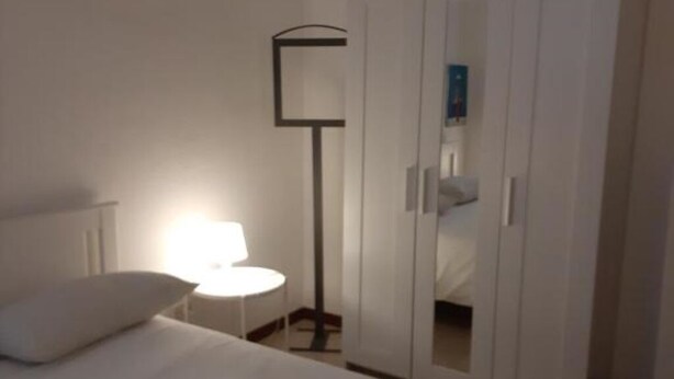 Ett sovrum med en säng, ett sängbord, en lampa och en garderob.
