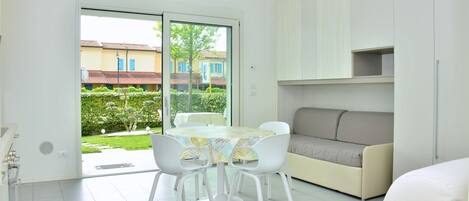 A modern living room with a sofa, a dining table with chairs, and a sliding glass door leading to a garden.