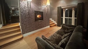 Una sala de estar moderna con chimenea, papel tapiz estampado y una escalera que lleva a otro nivel.